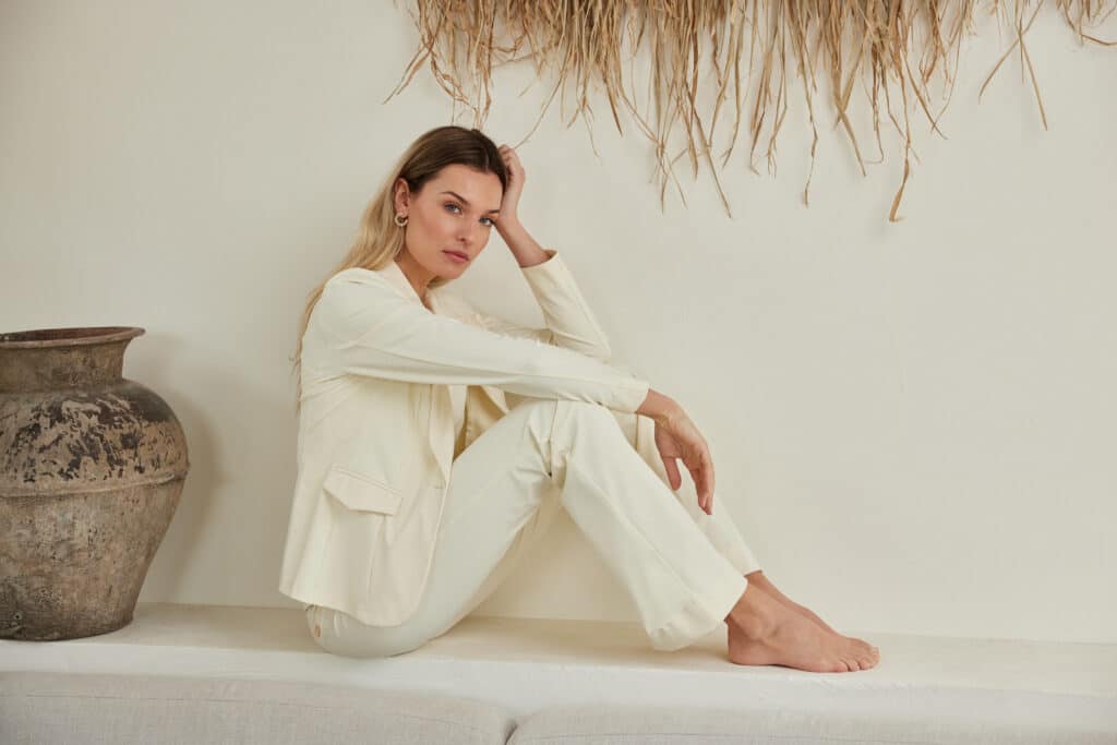 Woman wearing a light Aime Balance suit sitting on a white wall