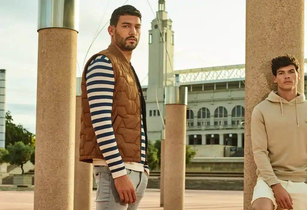 Two men standing before a stadium showing the new sweaters and jeans of No Excess